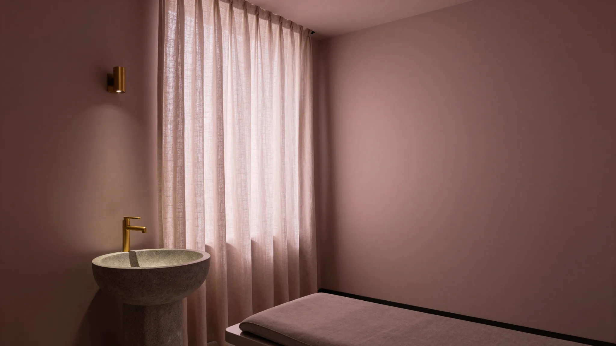 Treatment room with diffused daylight through linen, stone basin and brushed brass fixture